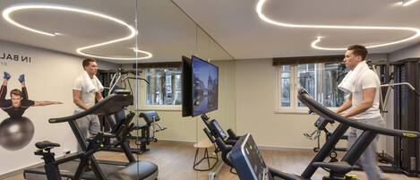 Un gimnasio con cintas de correr, bicicletas estáticas y una pantalla de televisión.