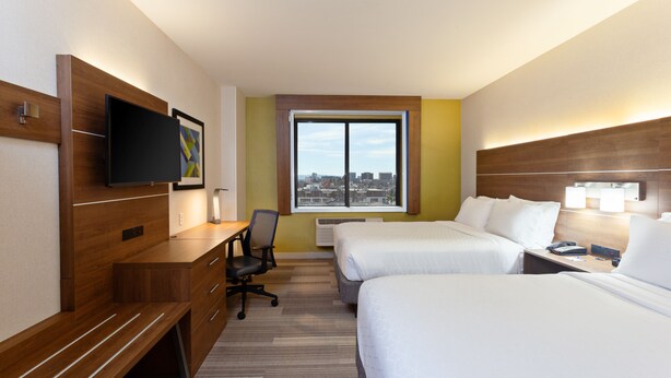 Une chambre d’hôtel avec deux lits, un bureau, une chaise, une télévision et une fenêtre donnant sur la ville.