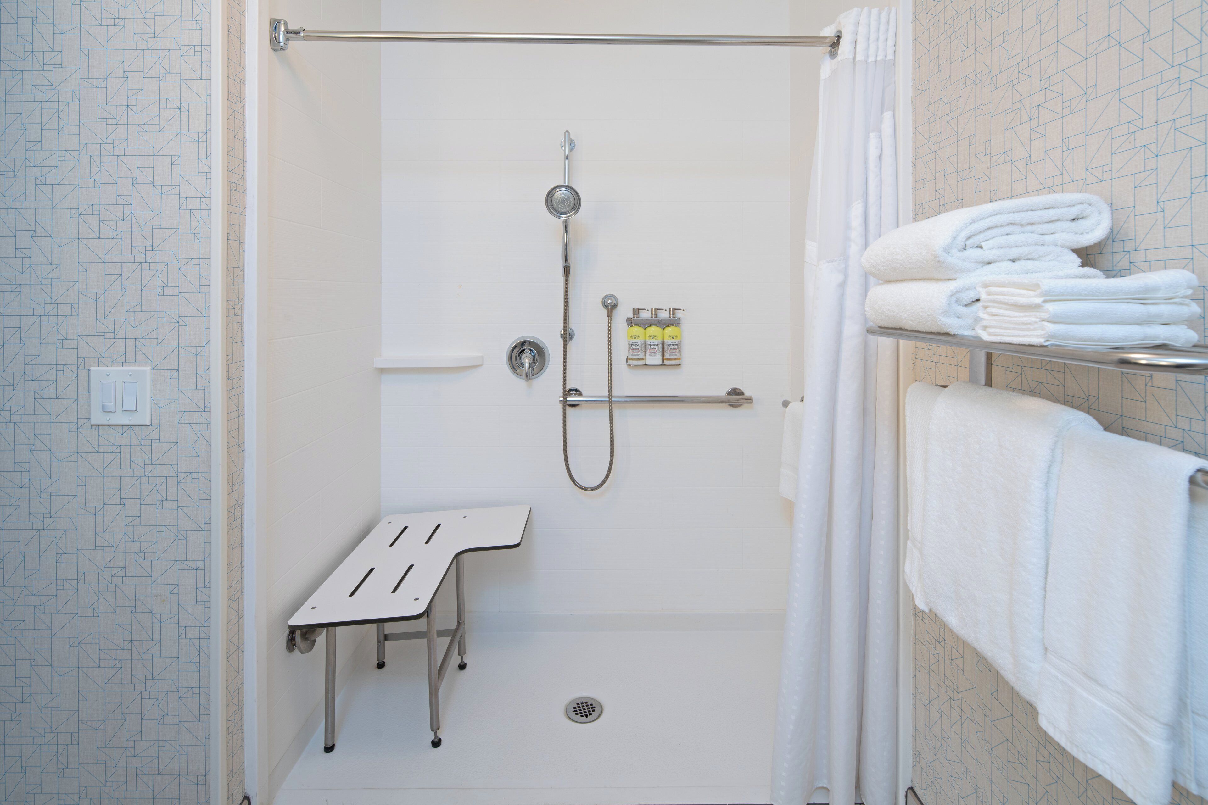 Eine bodenebene Dusche mit Handbrause, Duscharmatur und einer kleinen Sitzbank.