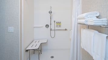 Eine bodenebene Dusche mit Handbrause, Duscharmatur und einer kleinen Sitzbank.