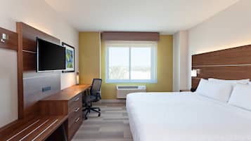 Habitación de hotel con una cama grande, un escritorio con silla, un televisor de pantalla plana y una ventana con persianas.