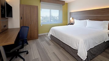 Habitación de hotel con cama, escritorio, silla, televisión, ventana y mesita de noche con lámpara.