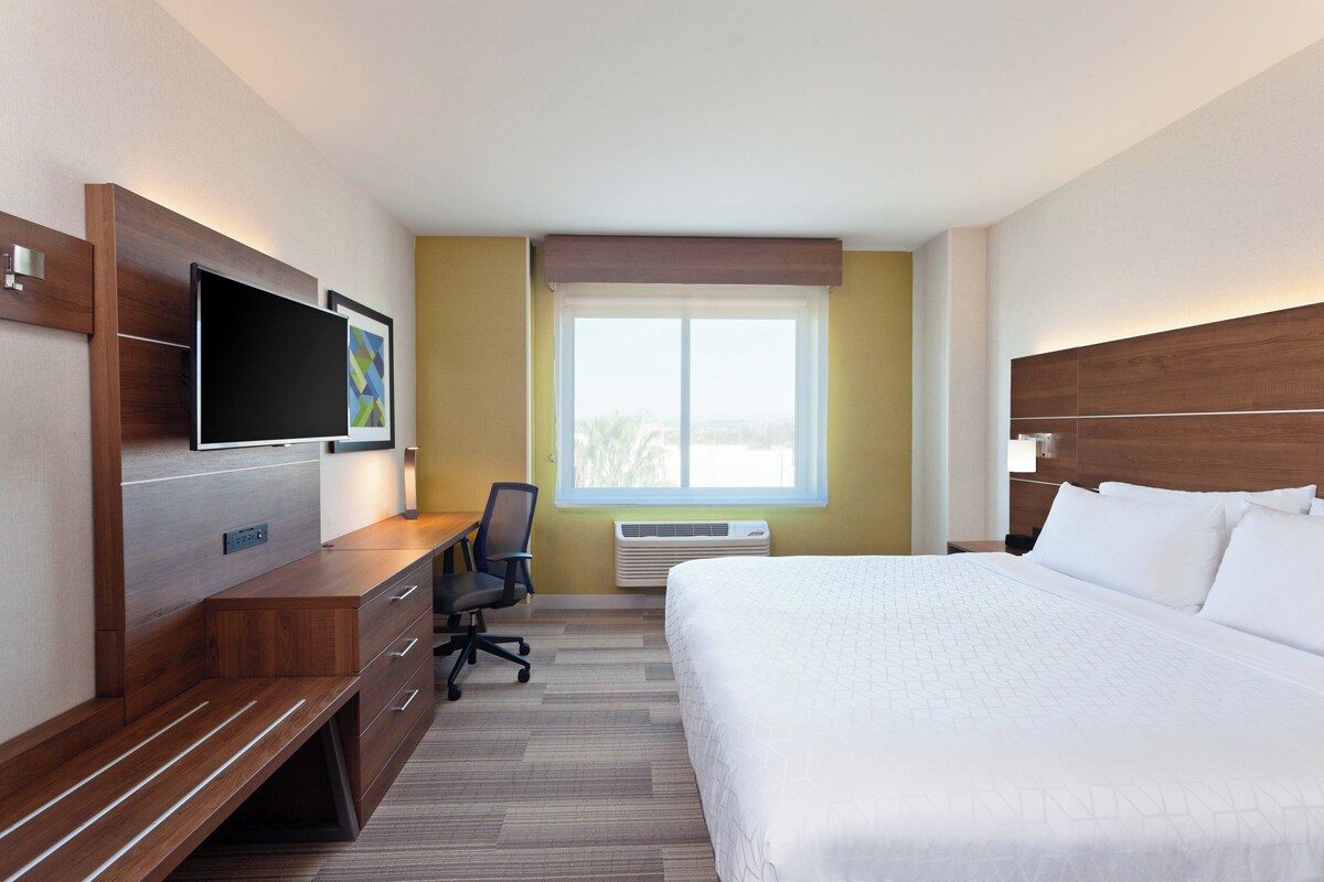 A hotel room with a bed, a desk, a chair, a TV, and a window.
