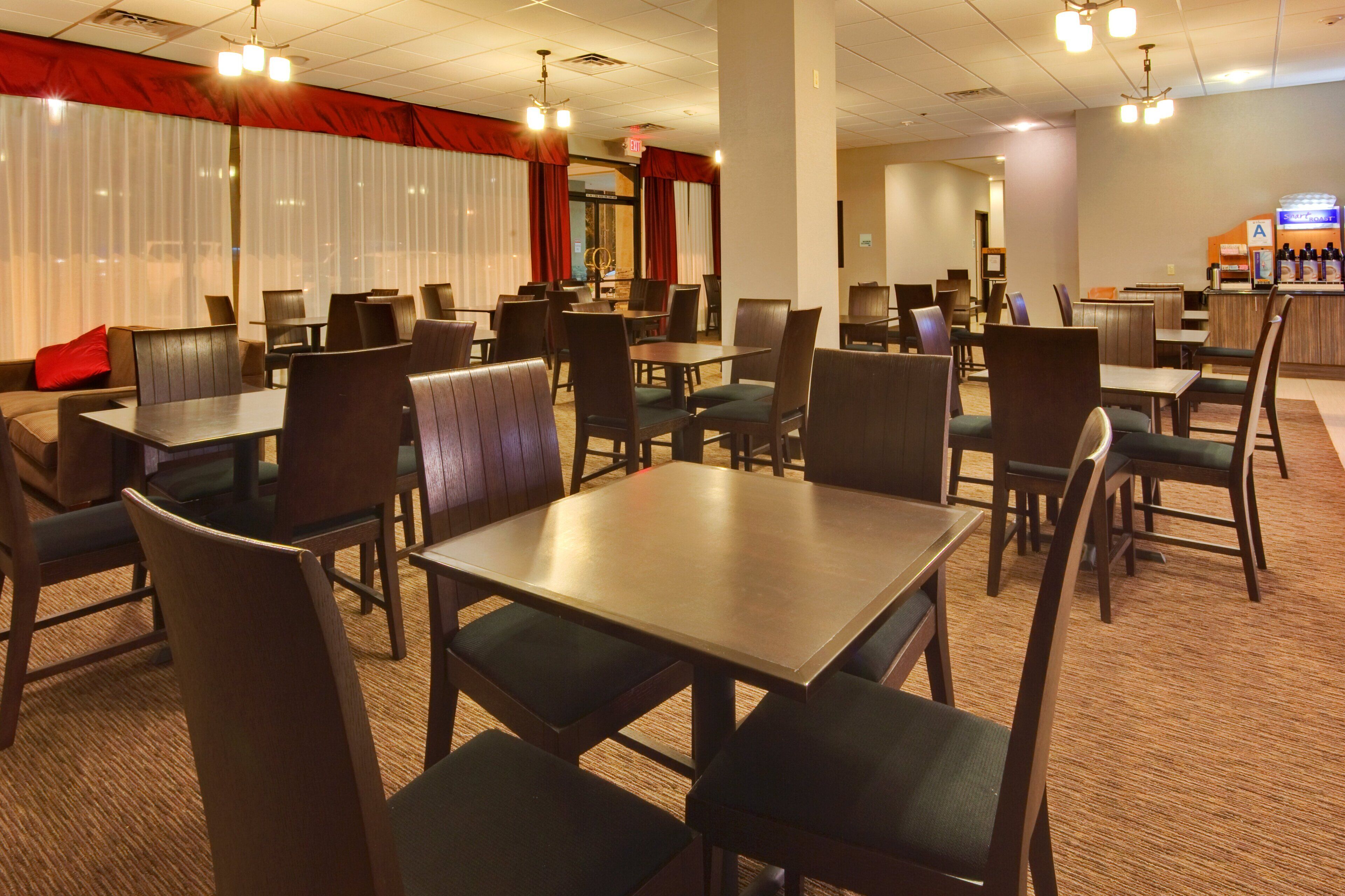 Un comedor de hotel con varias mesas y sillas, un bar y un telón rojo de fondo.