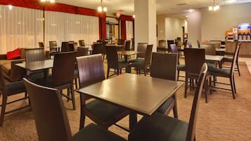 Un comedor de hotel con varias mesas y sillas, un bar y un telón rojo de fondo.