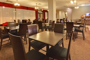 A hotel dining area with multiple tables and chairs, a bar, and a red curtain backdrop. - Holiday Inn Express Los Angeles Airport by IHG (Los Angeles)
