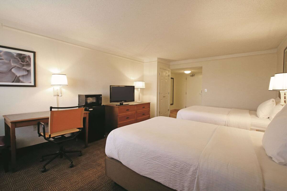 A hotel room with two beds, a desk with a chair, a television, and two lamps.