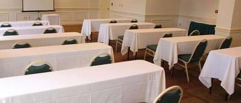 A conference room with multiple tables and chairs, a projector screen, and a carpeted floor.