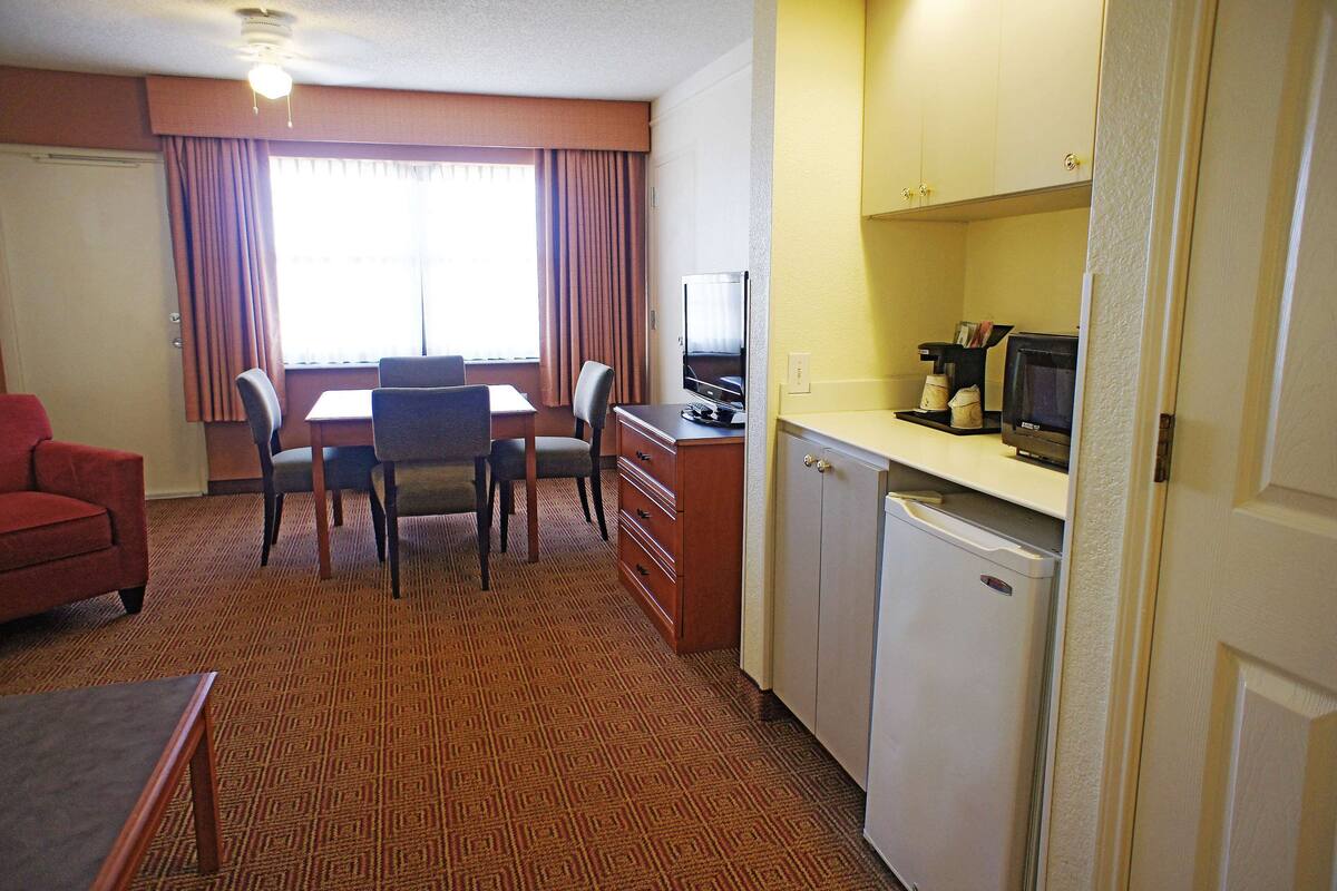 A hotel room with a dining table, chairs, a TV, a mini-fridge, and a red sofa.