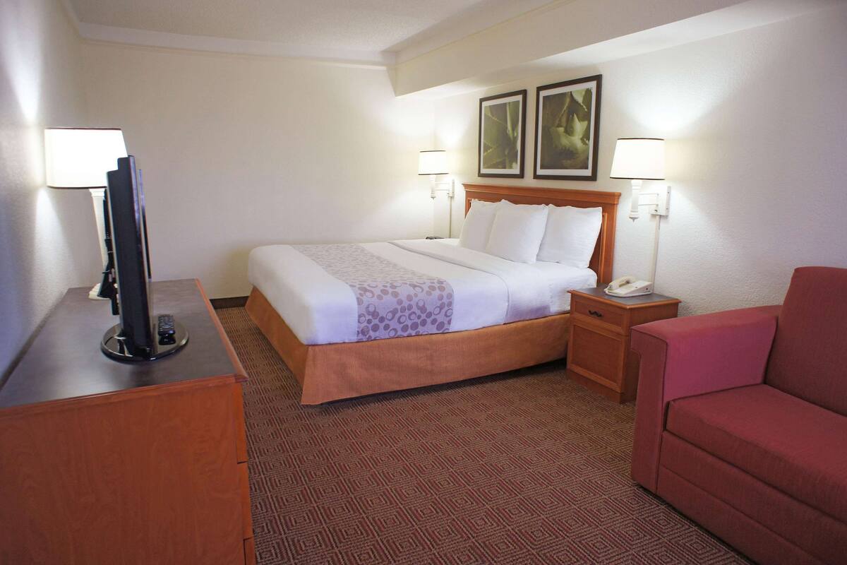 A hotel room with a bed, bedside tables, a TV, and a red couch.