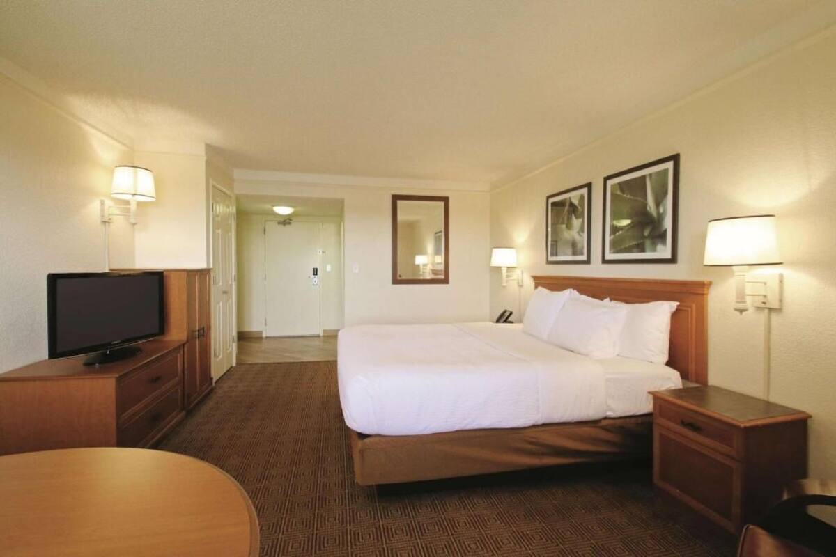 A hotel room with a bed, bedside tables, a TV, a desk, and a chair.