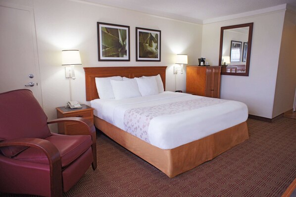 Habitación de hotel con una cama grande, cabecera de madera, dos lámparas de pared, un sillón rojo, una mesita de noche con un teléfono y un espejo en la pared.