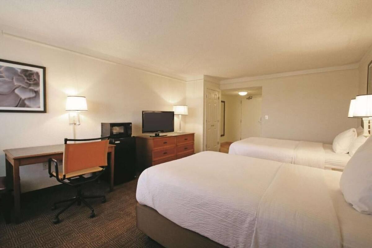 A hotel room with two beds, a desk with a chair, a television, and a lamp.