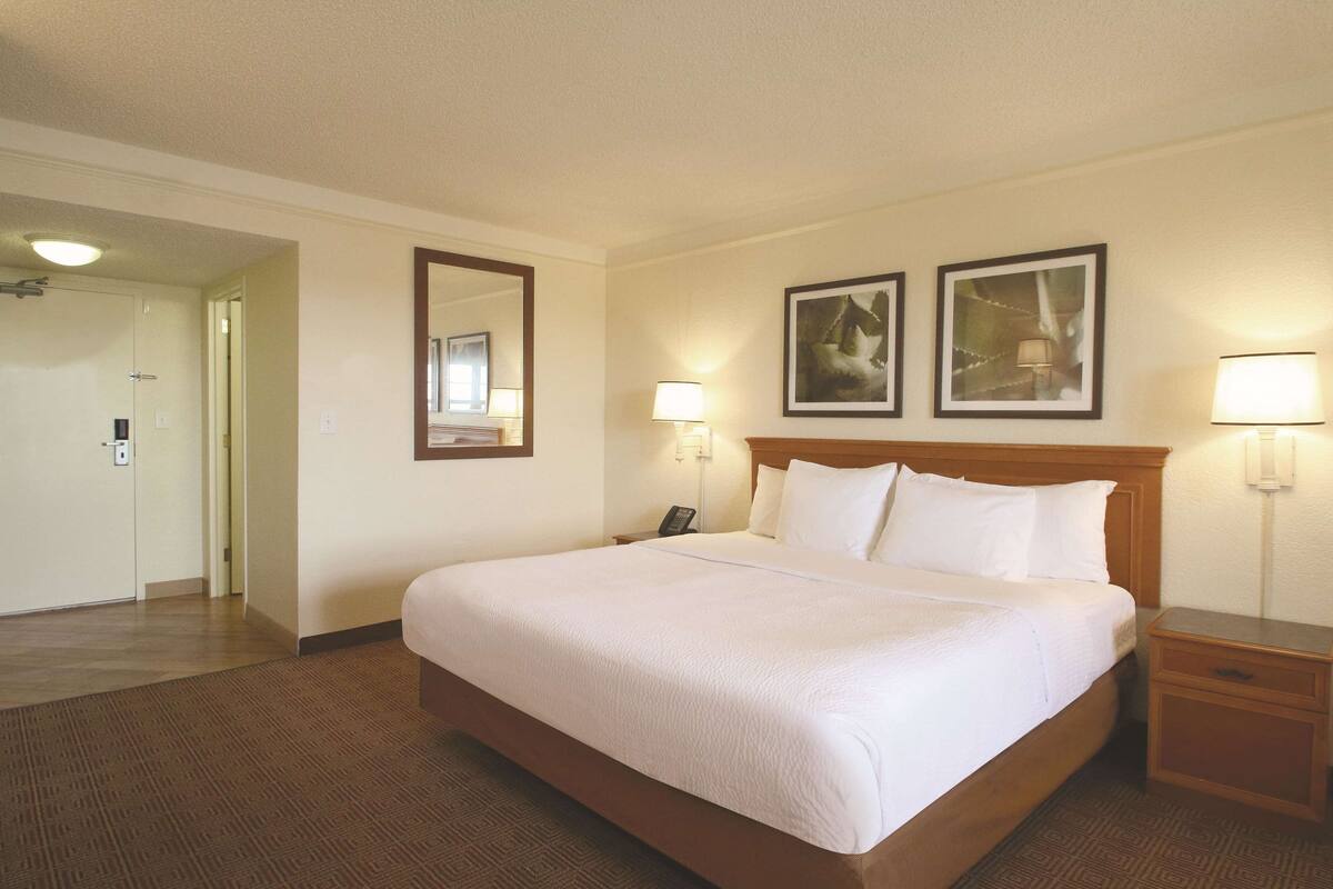A hotel room with a large bed, two bedside lamps, a nightstand, a wooden headboard, and two framed pictures on the wall.