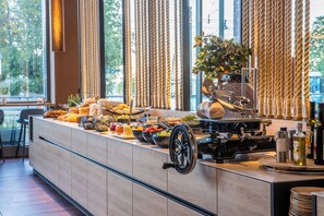 A buffet area with a variety of food items, a coffee machine, and a large window with curtains.