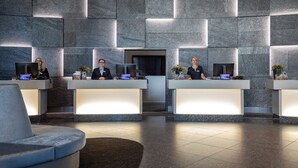 A reception area with two receptionists, a modern design, and a large stone wall. - ScanHotels City (Rostock)
