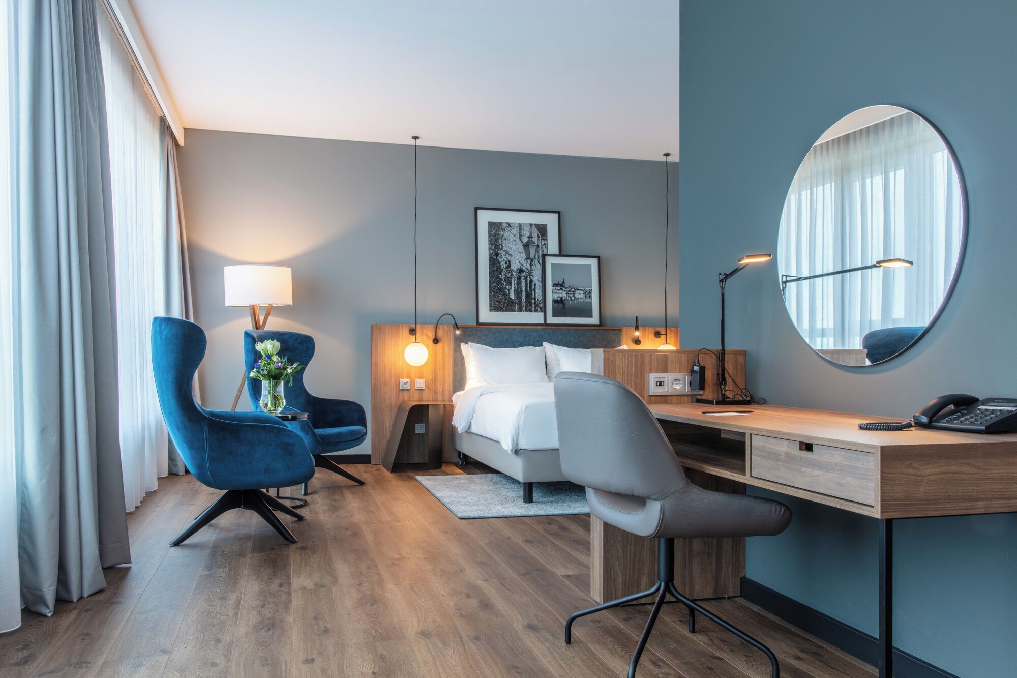 Habitación de hotel con cama, escritorio, dos sillas, espejo e imagen colgada en la pared.