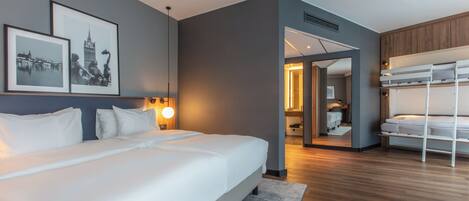 A modern hotel room with a large bed, a bunk bed, and framed pictures on the wall.