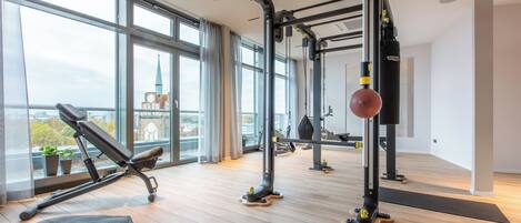A modern gym with exercise equipment, large windows, and a view of a cityscape.