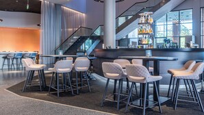 A modern bar area with high stools, a staircase, and a bar counter with bottles. - ScanHotels City (Rostock)