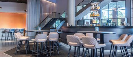 A modern bar area with high stools, a staircase, and a bar counter with bottles.