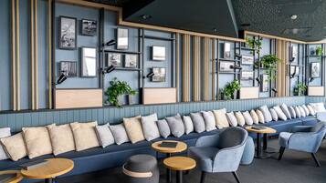 A modern lounge area with a blue sofa, grey and beige cushions, and round wooden tables.