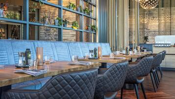 A restaurant with a long wooden counter, cushioned seating, and a wall adorned with potted plants.