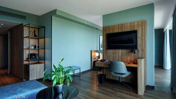 A modern living room with a wooden desk, a comfortable sofa, a flat-screen TV mounted on the wall, and a potted plant.