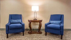 Two blue armchairs with matching cushions, a wooden side table with a lamp, and a patterned carpet. - Quality Inn Summerville - Charleston (Summerville)