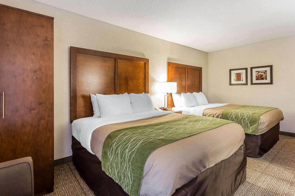 A hotel room with two beds, a wooden wardrobe, a lamp, and two framed pictures on the wall.
