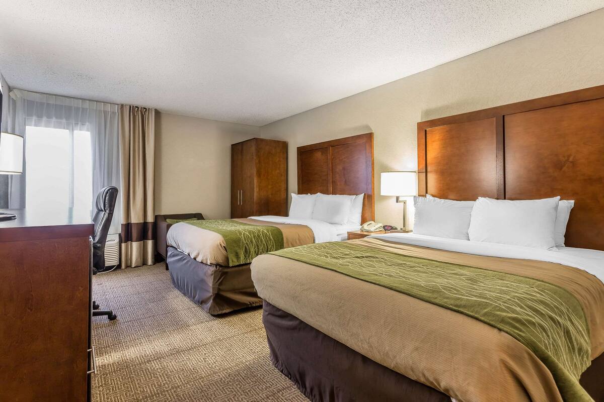 A hotel room with two beds, a desk, a chair, and a window with curtains.