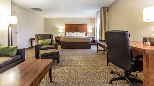 A hotel room with a bed, a desk, a chair, a sofa, and two bedside tables with lamps. - Quality Inn Summerville - Charleston (Summerville)