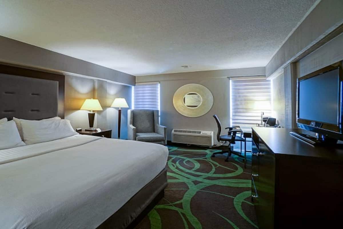 A hotel room with a large bed, a desk with a computer, a TV, a chair, and a circular wall decoration.