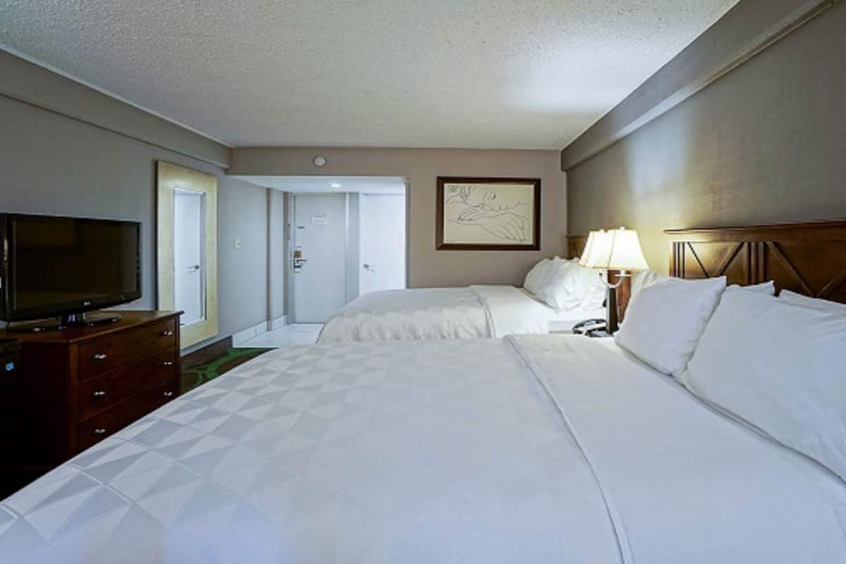 A hotel room with two beds, a television on a dresser, and a framed picture on the wall.