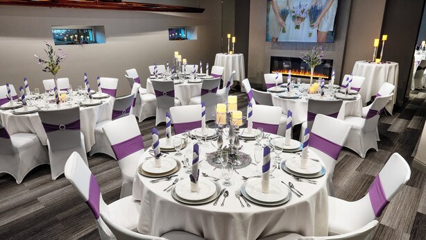 A banquet hall with round tables set for a formal event, featuring white tablecloths, purple sashes, and candles. - Holiday Inn Manhattan at the Campus by IHG (Manhattan)