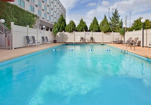 A swimming pool with clear blue water, surrounded by lounge chairs and a fence.