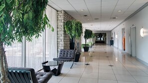 A corridor with a stone wall, potted plants, a seating area with a table and chairs, and a tiled floor. - Holiday Inn Manhattan at the Campus by IHG (Manhattan)