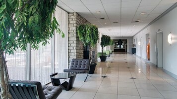Un pasillo con pared de piedra, plantas en macetas, un área de descanso con mesa y sillas, y piso de baldosas.