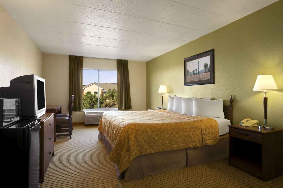 Een hotelkamer met een bed, een bureau met televisie, een stoel, een raam met gordijnen en een lamp op het nachtkastje.
