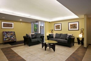 A lobby with two sofas, a glass coffee table, framed pictures on the walls, and a magazine rack.