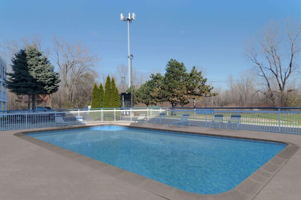 A rectangular swimming pool with a white fence, surrounded by trees and a life guard sign.