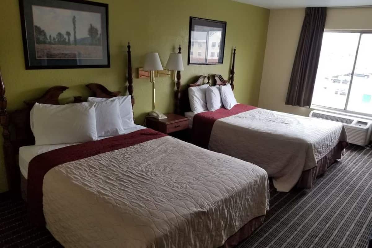 Een hotelkamer met twee bedden, een nachtkastje, een lamp en een raam met uitzicht.
