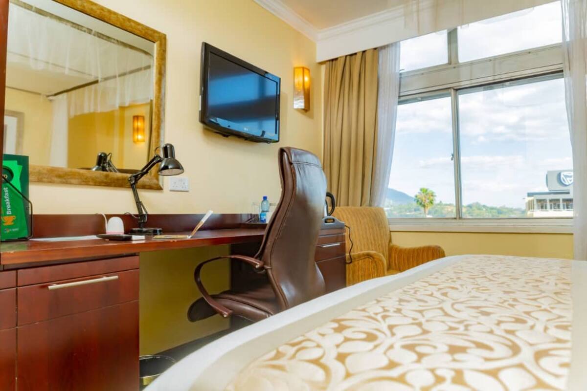 Habitación de hotel con cama, escritorio, silla, televisión y ventana con vistas.