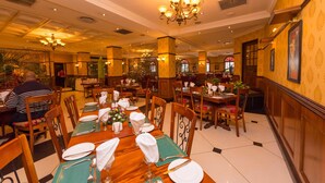 Un comedor con mesas dispuestas para el servicio, sillas de madera y una araña.