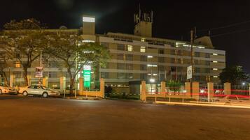 A multi-story hotel with a gated entrance, a signboard, and a street view with parked cars.