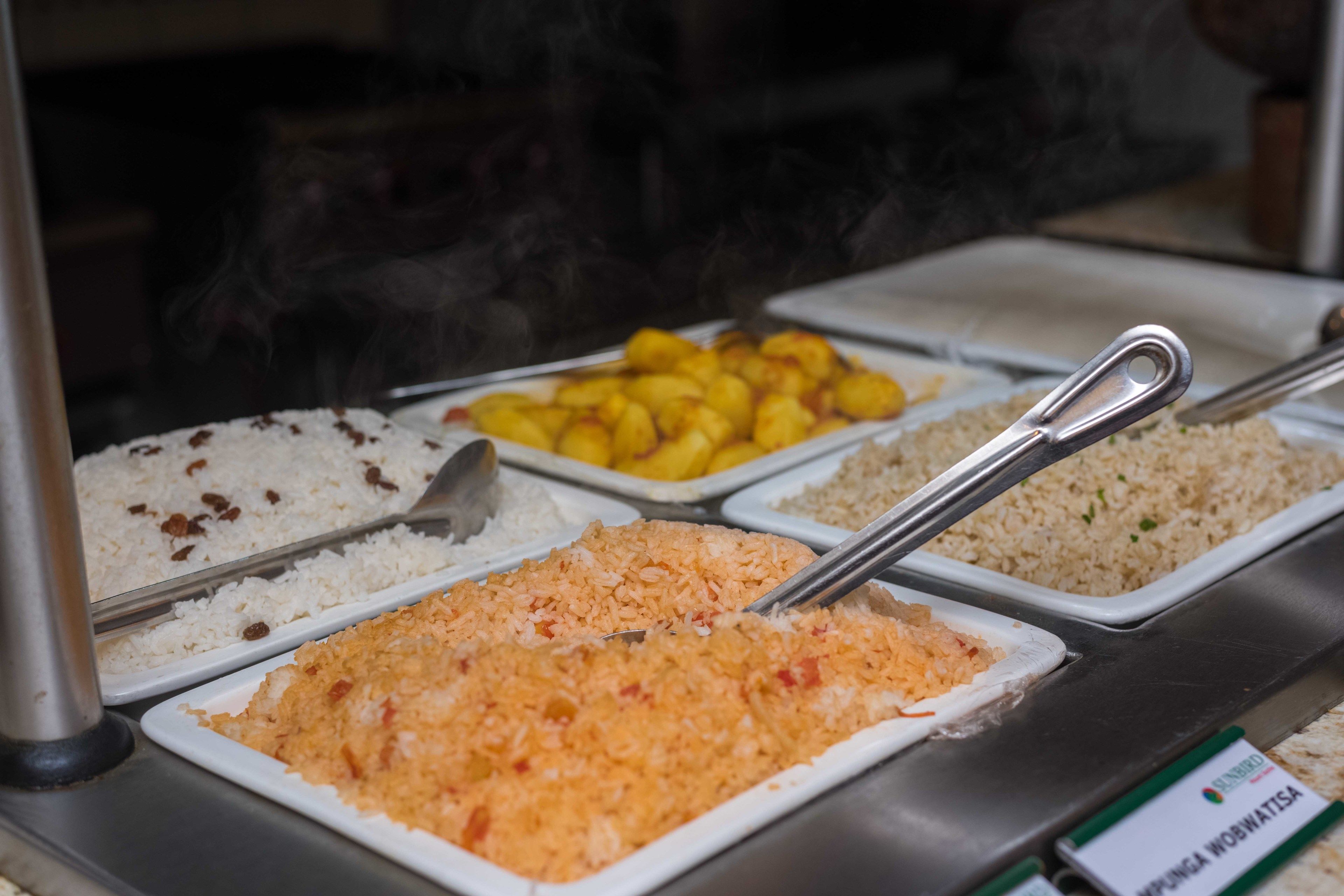A buffet with various food options including rice, orange-colored rice, and yellow fruit.