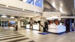 A hotel lobby with reception desks, a check-in counter, and a staircase leading to an upper level.