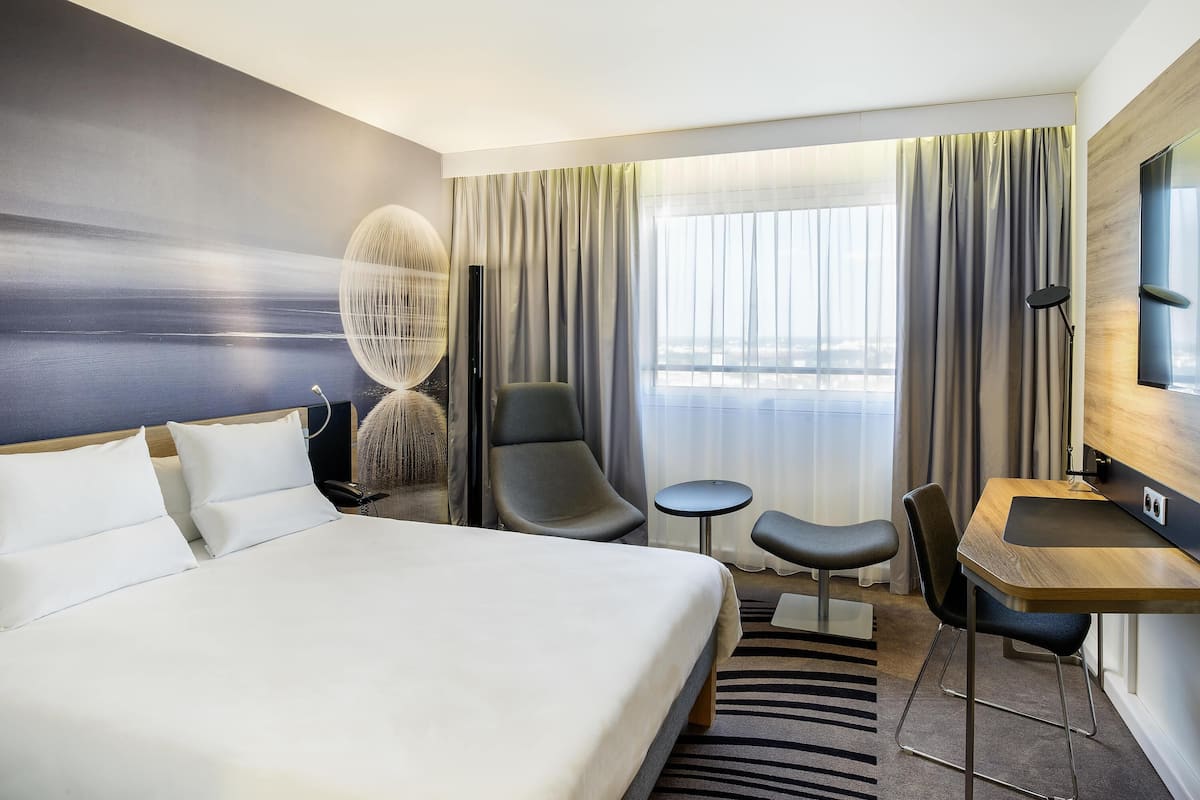 Ett modernt hotellrum med en stor säng, ett skrivbord, en stol och ett litet bord.