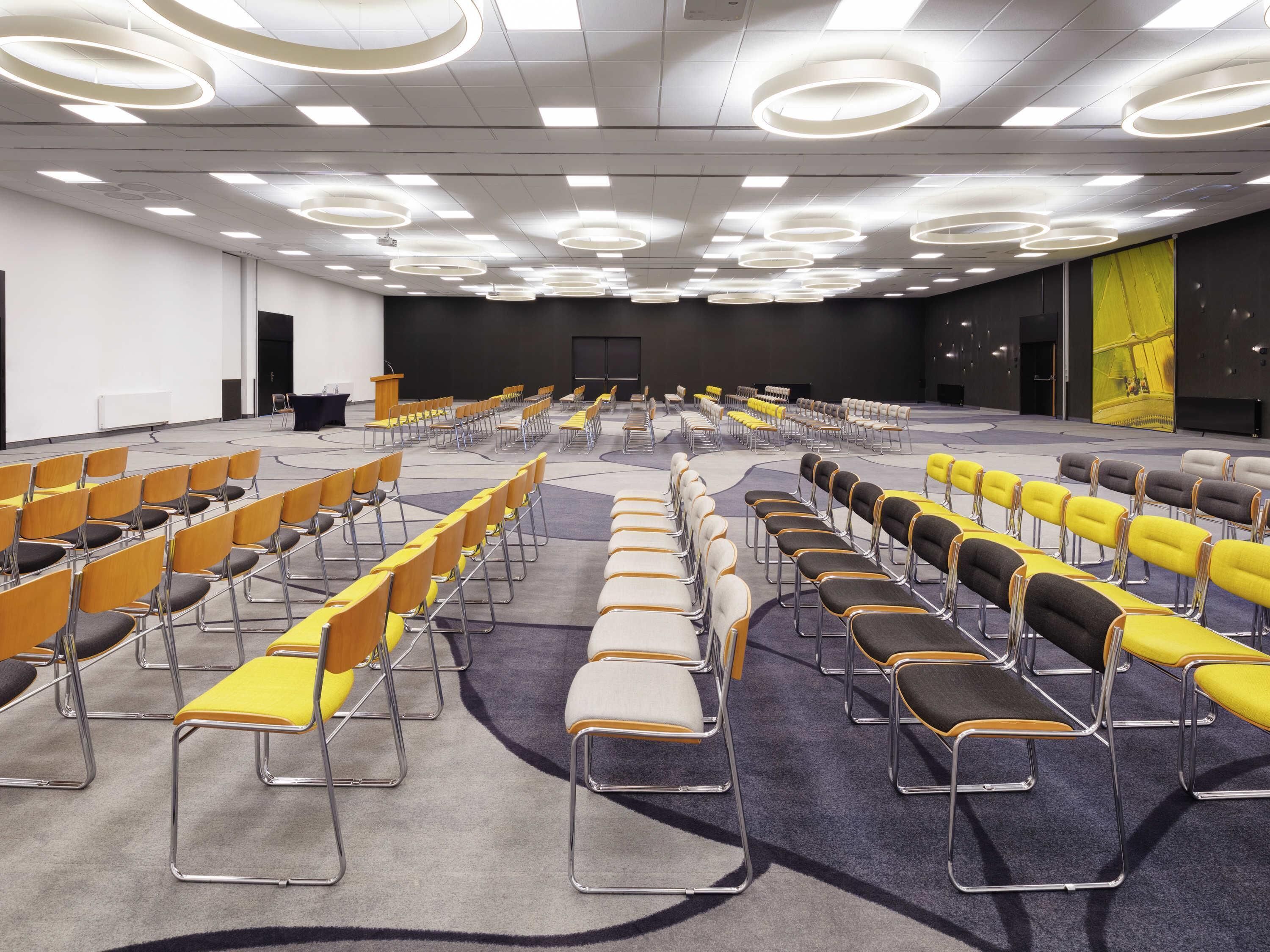 A conference room with rows of chairs, a podium, and a large screen.