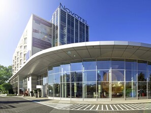 A modern hotel with a glass facade, a prominent 'NOVOTEL' sign, and a curved entrance canopy.